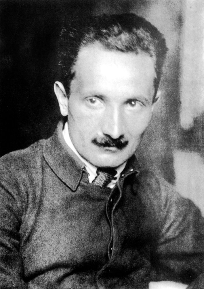 Martin Heidegger um 1920, als junger Mann im dunklen Anzug, mit ernstem Blick und kurzen, zurückgekämmten Haaren.